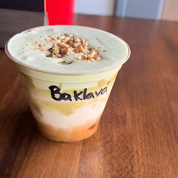 A Baklava drink from Plant City Comic Cafe, topped with whipped cream and nuts, on a wooden table.