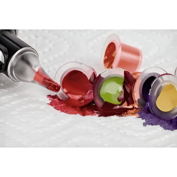 A tattoo gun with red ink and several spilled ink caps in various colors on a white surface.