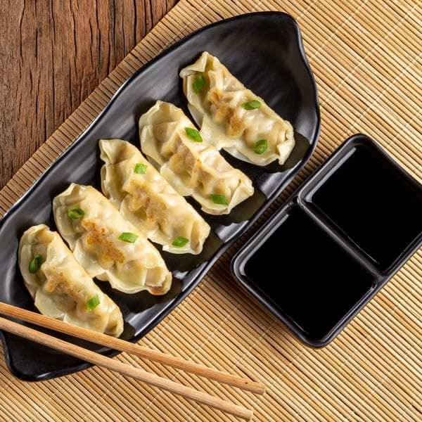 Pan-fried gyoza dumplings with green onions on a black plate, with soy sauce and chopsticks.