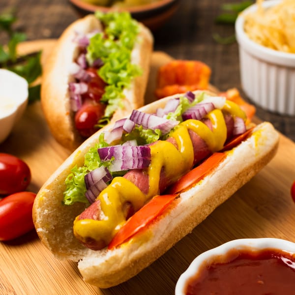 Two hot dogs with mustard, red onions, lettuce, and tomatoes on a wooden board.